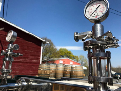 A close up of a metal wine filter with wine barrels in the background