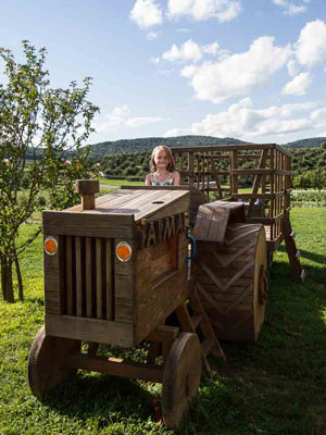 A small child pretends to steer a giant wooden tractor