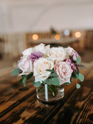 A flower arrangement of peach, ivory and pale purple flowers on a chestnut wood table.