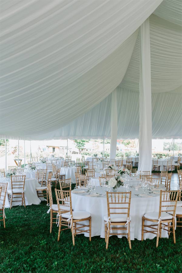 Tables with white tablecloths, and bamboo chairs under a fabric draped reception tent.