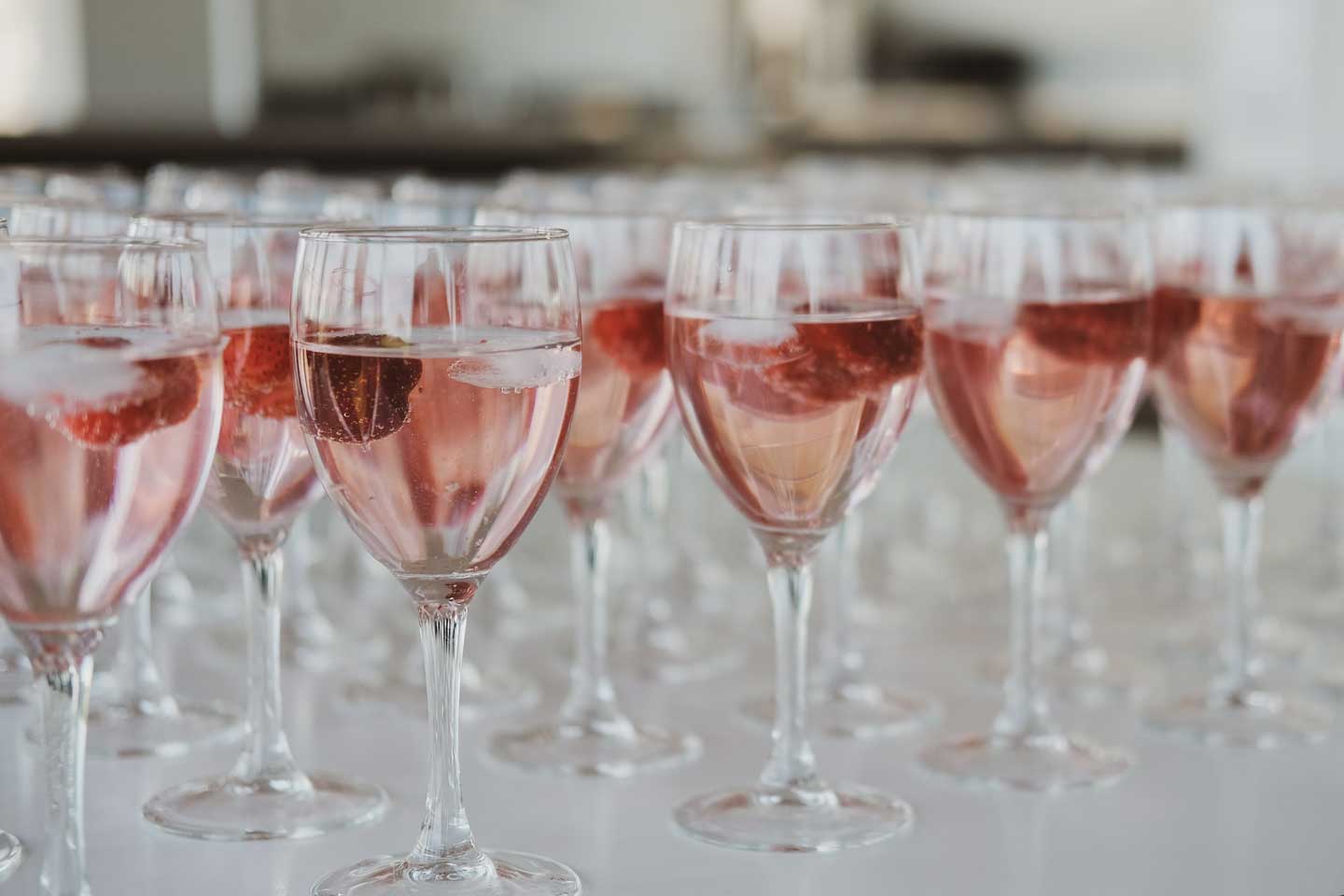 Airy and bright lighting with rows of Wine Glasses filled with pale pink colored wine.