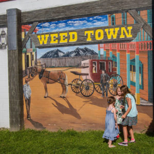 Three girls stand in front of a western themed mural with a cowboy and horse