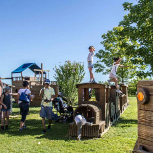 a large wooden train surrounded by children playing on it.