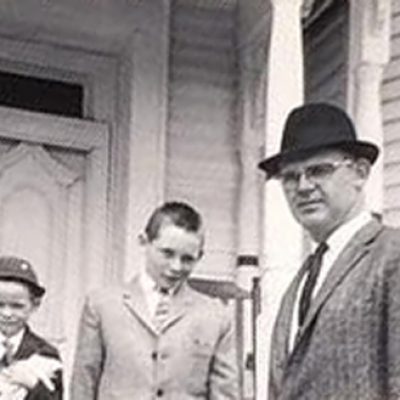 A father and two sons stand on their front porch dressed in suits.